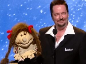 Man in suit holding puppet with red bows.