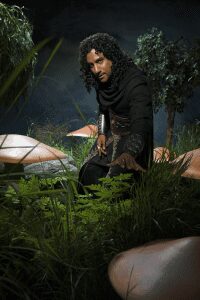 Person in dark attire among oversized mushrooms.