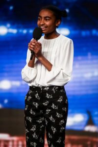 Young girl singing into a microphone on stage.