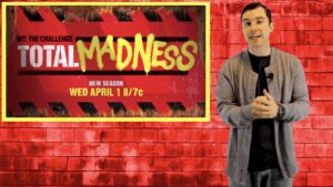 Man standing beside "Total Madness" poster.